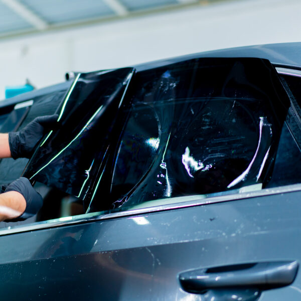 a car mechanic carefully sticks a protective tinted film on a car glass at detailing station